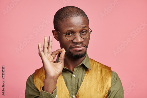 Indoor picture of confident serious male with dark pure skin makes ok gesture, being satisfied with everything, hasn`t any rejections. Satisfied Afro American man isolated over pink background