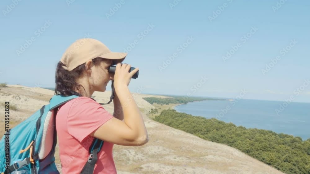 Travel woman looking at wildlife with binoculars. Woman on vacation looking at nature landscape. Hiker with a backpack is looking through binoculars at sea, at beautiful landscape. Mountain. Beach. Travel woman looking at wildlife with binoculars. Woman on vacation looking at nature landscape. Hiker with a backpack is looking through binoculars at sea, at beautiful landscape. Mountain. Beach.