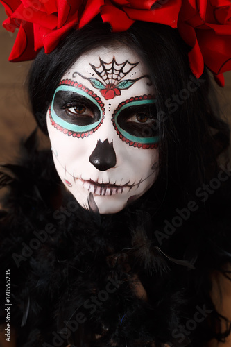 Day of the dead. Halloween. Young woman in day of the dead mask skull face art and rose. Dark background.