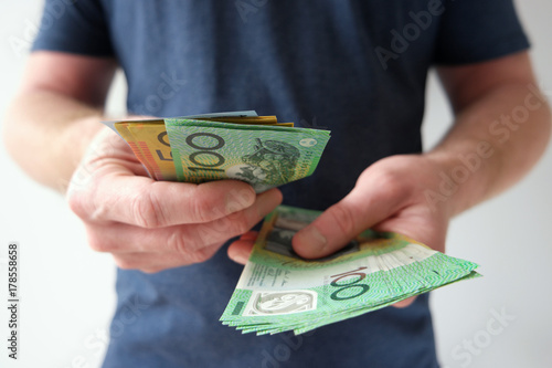 A man counting hundred and fifty Australian dollar bills in cash on hand as payment, savings, business funds, dividends, wealth.