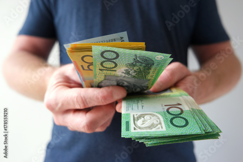 A man counting hundred and fifty Australian dollar bills in cash on hand as savings, payment, dividends, funds, investment.