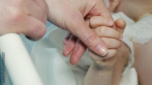 Close up of a young mother and sick child holding hands for comfort in a hospital bed