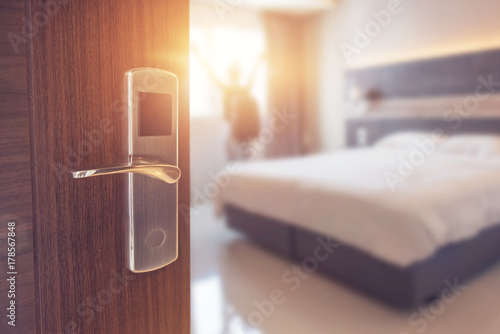 Opened door of hotel room in morning with background blurred happy backpacker traveller stay in hotel, sunlight effect.