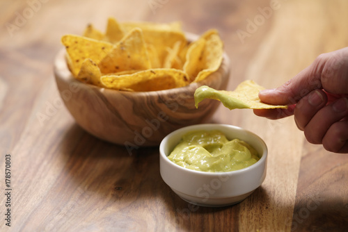 young female hand dipping nachos in guacamole sauce