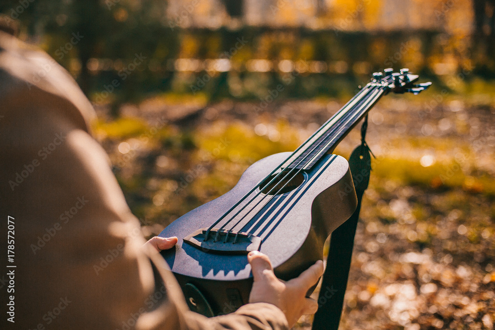 Closeup of young man hands playing acoustic bass guitar ukulele at the park sit Enjoy living Sunshine in the evening.