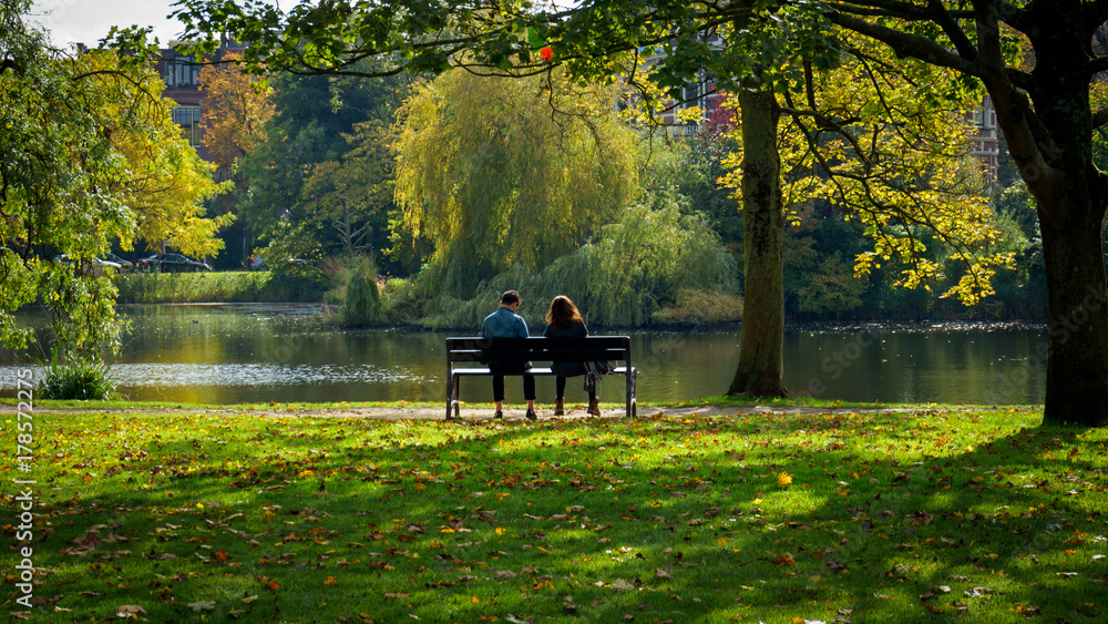 © Maksims - couple of woman and man sitting on the bench in autumn sunny park