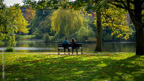 couple of woman and man sitting on the bench in autumn sunny park
