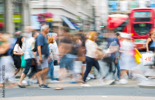 Piccadilly circus with lots of people, tourists and Londoners crossing the junction. Red bus at the background. Blurred type image. London, UK