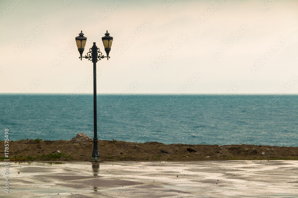 The lamppost standing on the embankment on the background of sea in rainy day