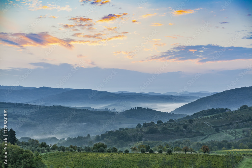 Beautiful sunrise with some fog between the hills with vineyards in Tuscany in Italy