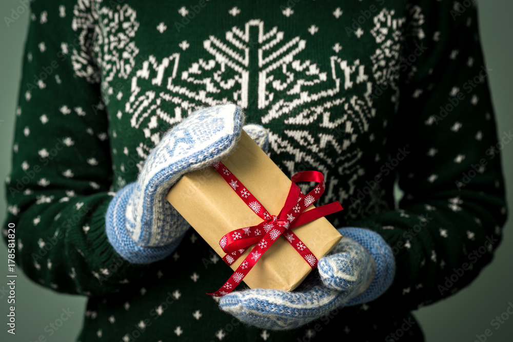 Christmas background. Girl is holding a Christmas present. Gifts for men. Merry Christmas. Gift for a girl. Sweater with Christmas ornament. Knitted dress. Box with gifts. Image in a dark key.