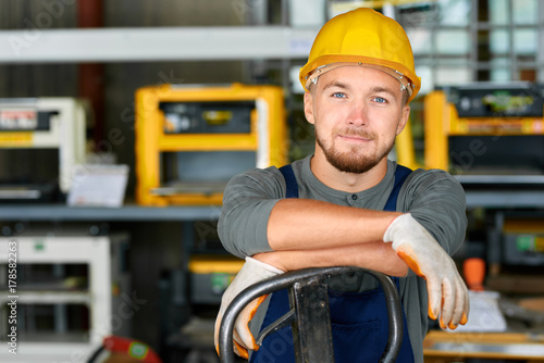 Portrait of cheerful young worker wearing hardhat posing looking at camera and smiling enjoying work at modern factory