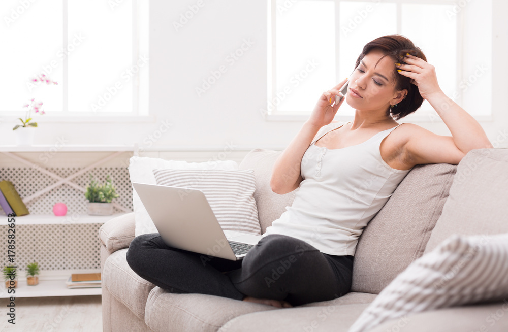 Pensive girl with laptop and mobile sitting on beige couch Pensive girl with laptop and mobile sitting on beige couch