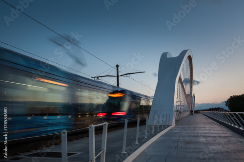 Fahrende Bahn mit sichtbarer Bewegungsgeschwindigkeit über die Beatus-Rhenanus-Brücke in Kehl zur blauen Stunde
