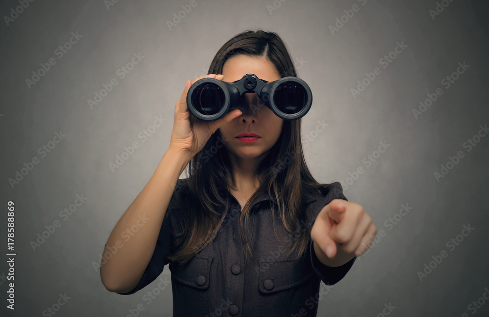 Young woman looking through binoculars and showing ahead by her index finger. Find and search. Find something interesting. Young woman looking through binoculars and showing ahead by her index finger. Find and search. Find something interesting.