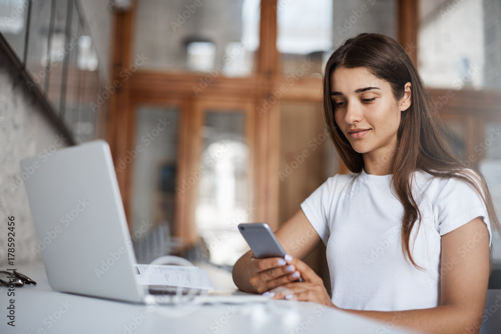 Young happy woman using a smart cell phone to look at her selfies to pick a new social media profile picture. Young happy woman using a smart cell phone to look at her selfies to pick a new social media profile picture.