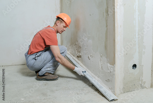 Worker is putting a gypsum plaster on a wall. He is using a long rule.