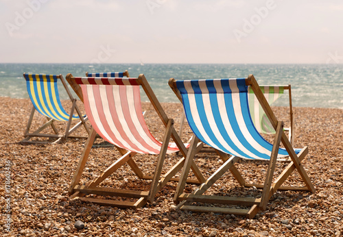 Classic red, blue, green and white striped deckchairs on the beach, the sea in the background in warm evening light