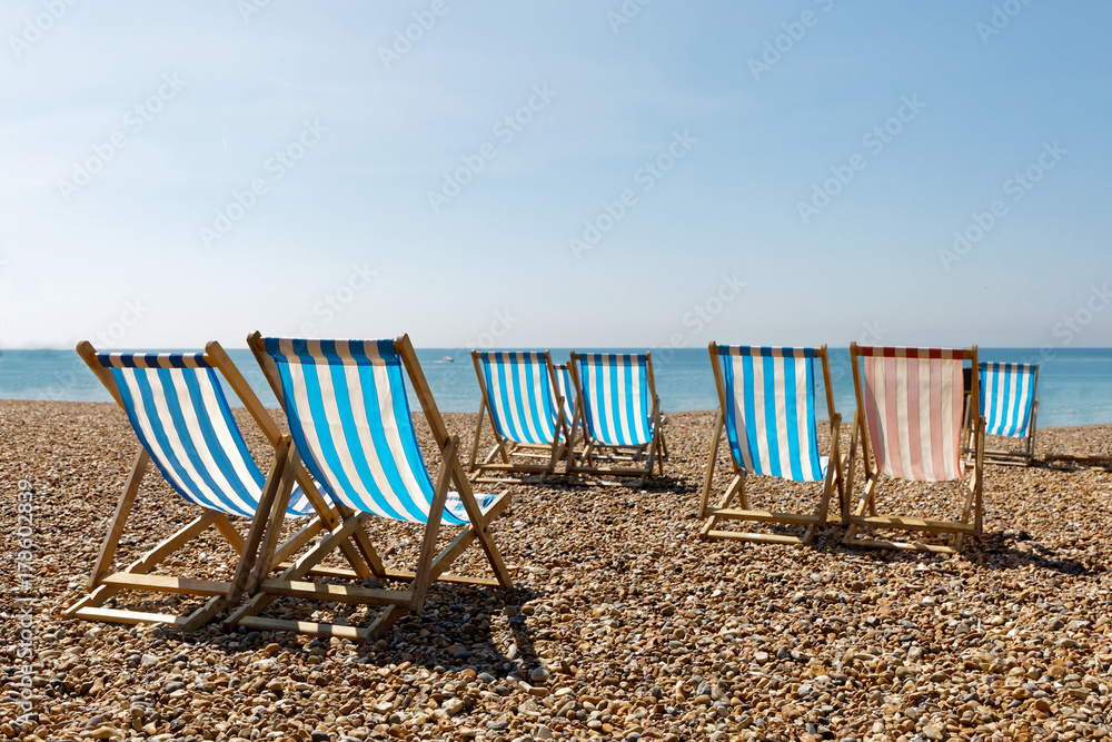 Colorful empty red and blue deckchairs on the beach, blue sea in the background