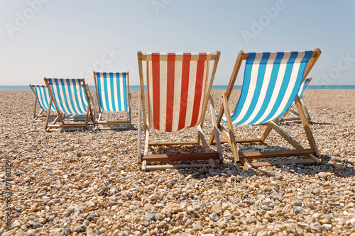 Peaceful day on the pepple beach, classic red and blue deckchairs, blue sea in the background