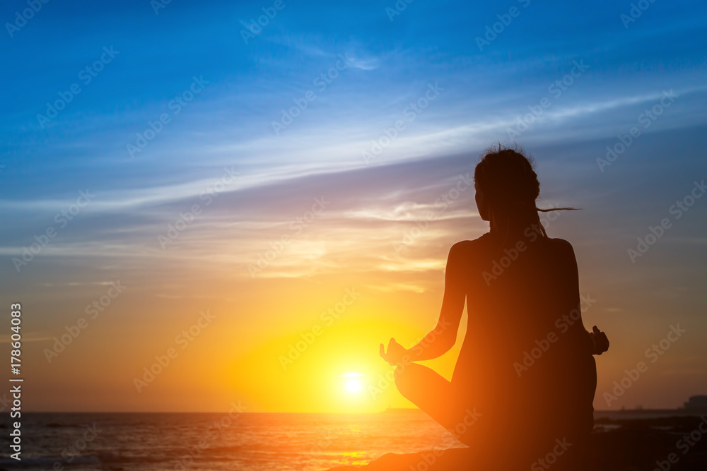 Yoga woman silhouette meditation at the sea beach during amazing sunset.