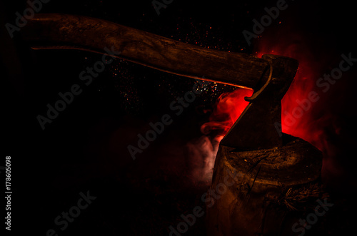 Fotografie Old ax attached to the tree trunk on horror red foggy background