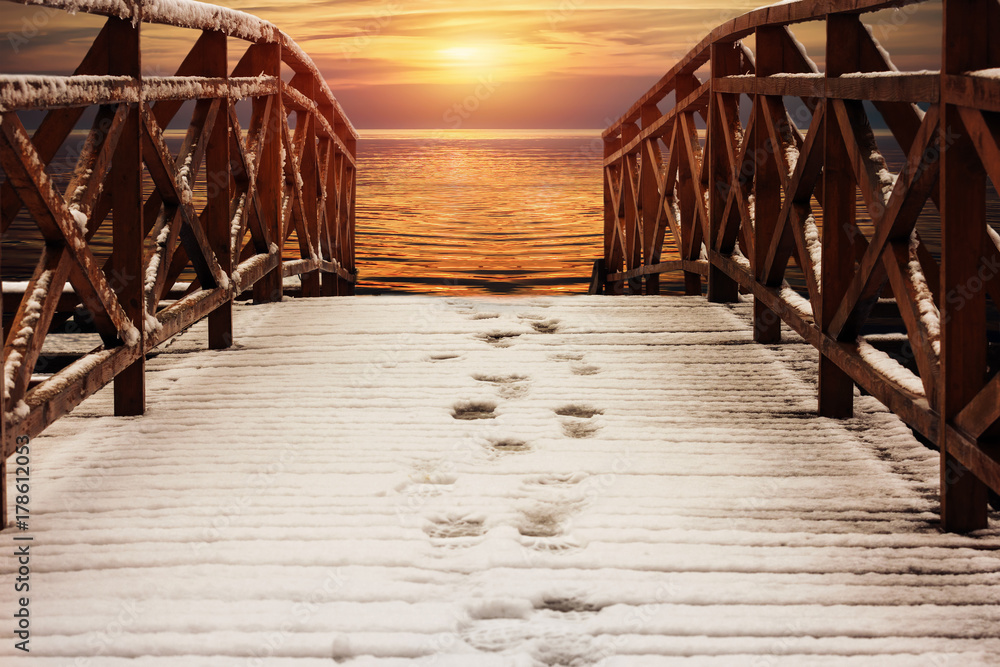 Fototapeta premium wooden walkways, pier, covered with snow, lead to the river at sunset