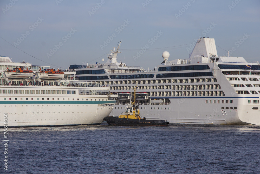A huge cruise ships being manouvered and reversed towards high sea by pilots and tugboats