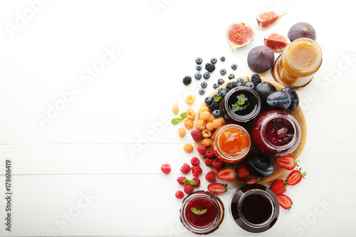 Glass jars with different kinds of jam and berries on wooden table photo