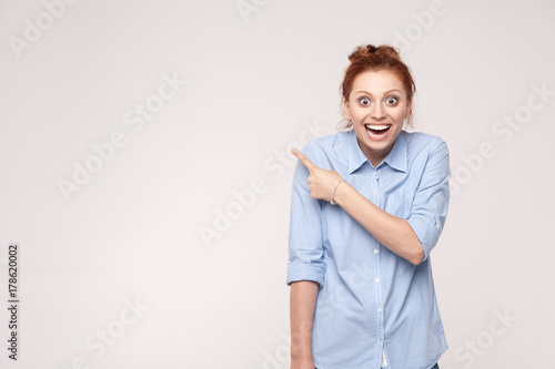 Wow! Handsome redhead woman in shoked. Pointing away while standing isolated on gray background