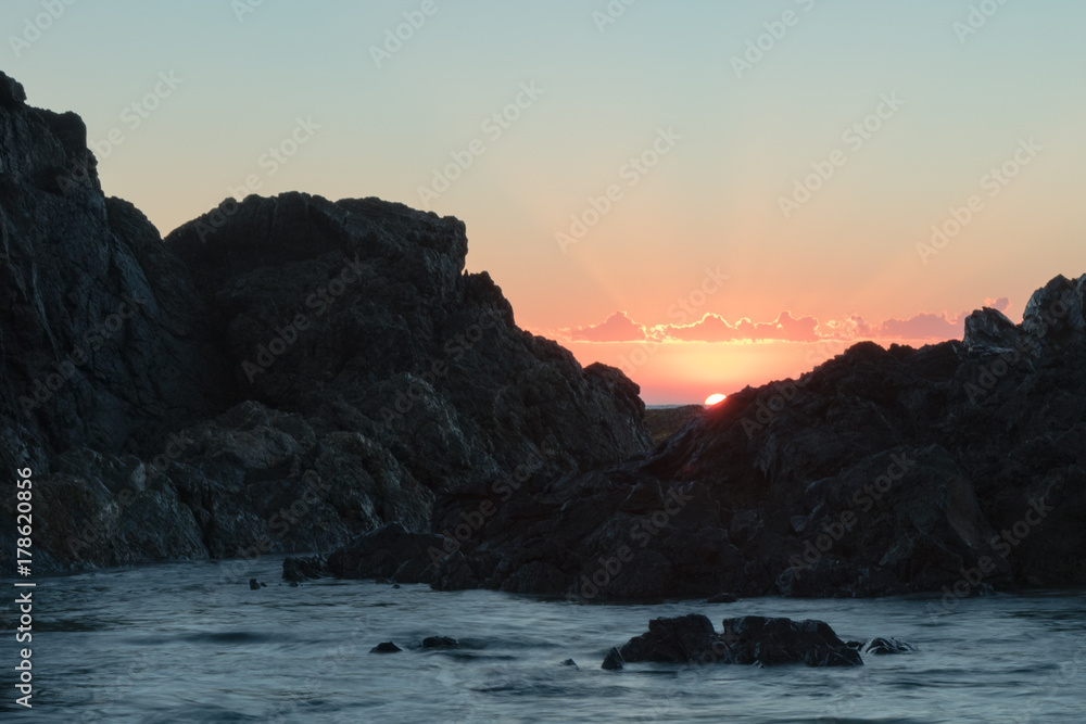 sun peaking over the rock over the ocean