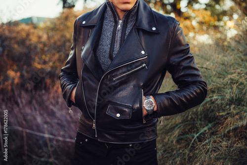 Man wearing black leather jacket and watch posing outdoors