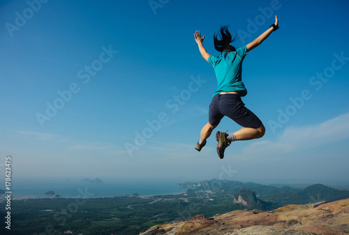  joyful woman hiker jumping on rocky mountain top