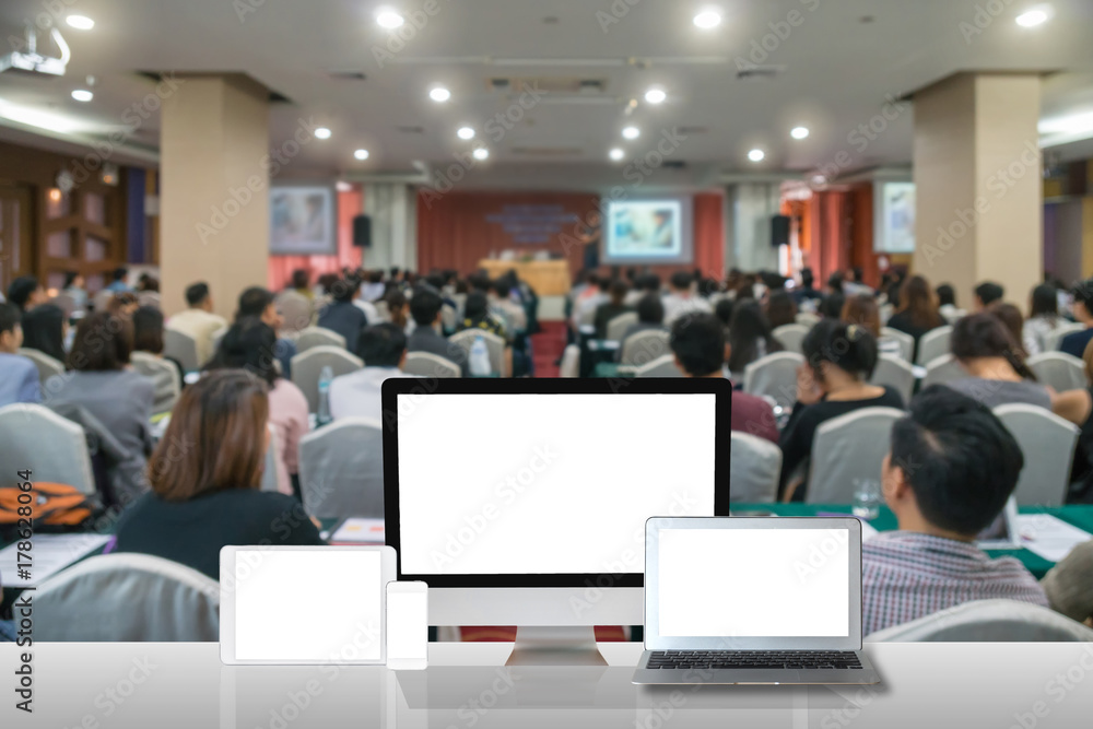 Computer set show on the white table over the Abstract blurred photo of conference hall or seminar room with attendee background, business technology and education concept