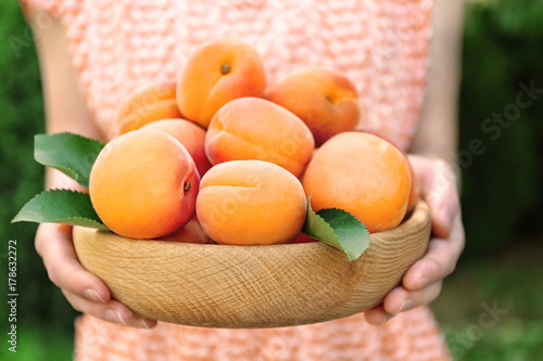 Woman holding bowl with juicy ripe apricots outdoor