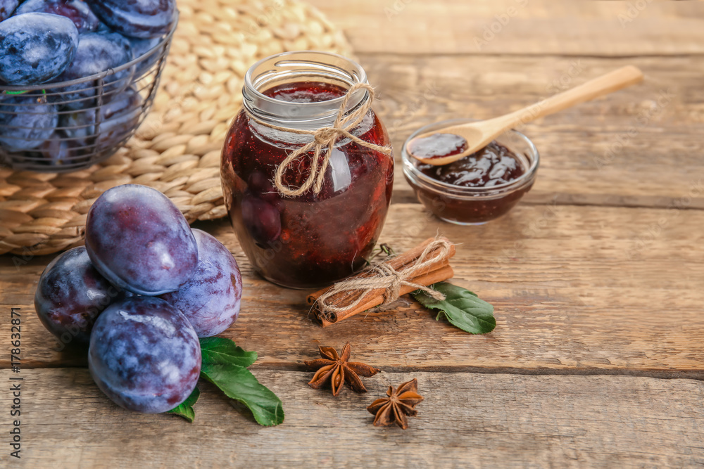 Composition with ripe plums and delicious jam on wooden background