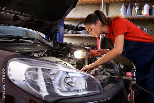 Young female mechanic repairing car in body shop
