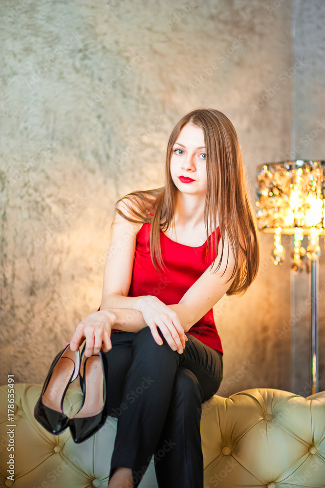 Beautiful young girl in a red top and black trousers. Girl on the background of a beautiful wall and a lamp tube