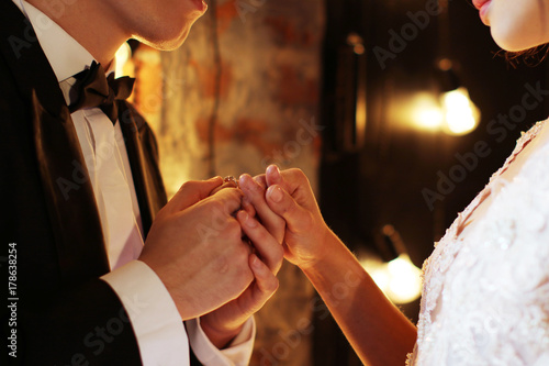 Newlyweds exchange rings, groom puts the ring on the bride's hand in marriage registry office. Dark brown background photo