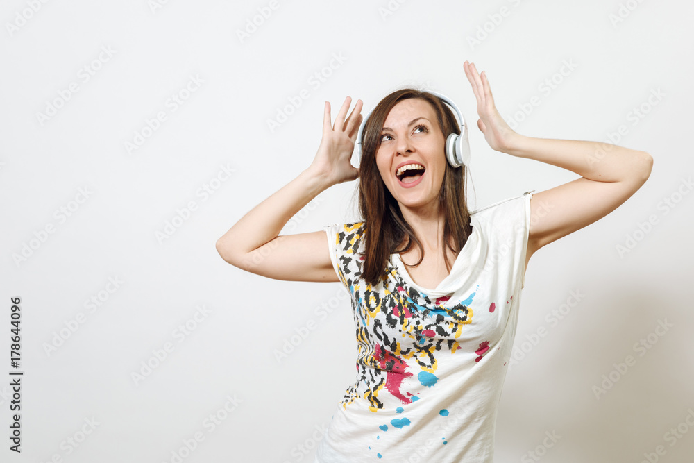 Beautiful emotional European young happy brown-haired woman with healthy clean skin and charming smile, dressed in casual light clothes, listens and enjoys music on headphones on a white background. Beautiful emotional European young happy brown-haired woman with healthy clean skin and charming smile, dressed in casual light clothes, listens and enjoys music on headphones on a white background.