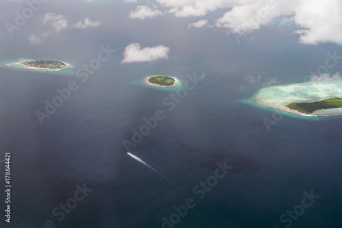 Tropical islands and atolls in Maldives in Indian Ocean from aerial view. Cutting wave boat. Piece of paradise on the Earth. Good choice for vacation. Beautiful top view for wallpaper.