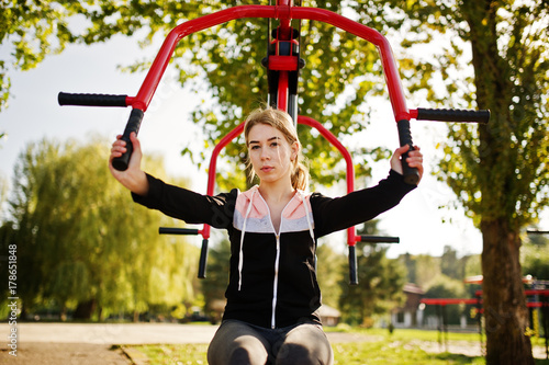 Young girl has the training and doing exercise outdoors on street simulators. Sport, fitness, street workout concept.