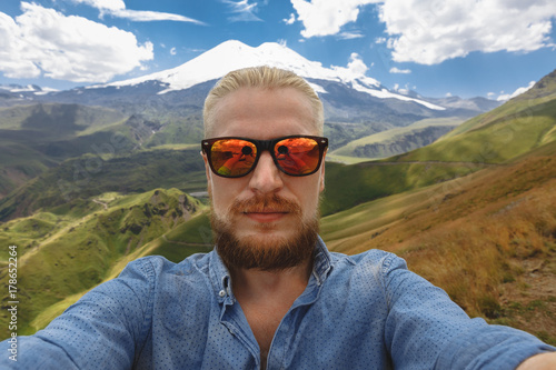 Young Traveler Man Makes Selfie On Background Of Mount Elbrus. Adventure Destionation Journey Concept photo