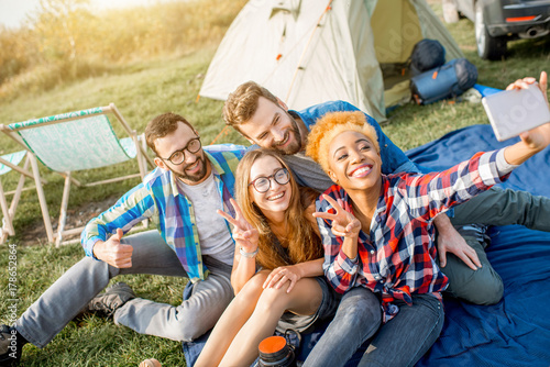 Multi ethnic group of friends dressed casually having fun making a selfie photo together during the outdoor recreation with tent, car and hiking equipment near the lake © rh2010