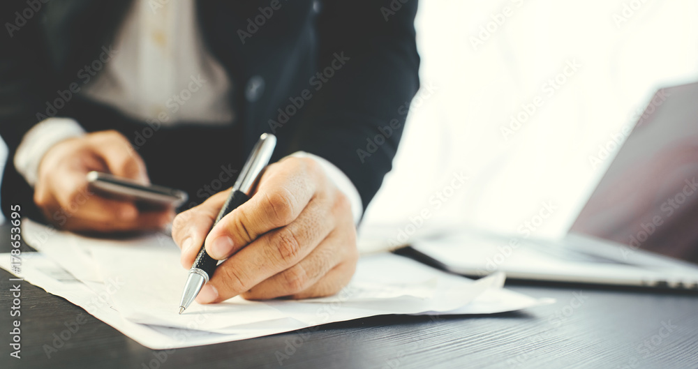 Side view shot of a man's hands using smart phone in interior, rear view of business man hands busy using cell phone at office desk Side view shot of a man's hands using smart phone in interior, rear view of business man hands busy using cell phone at office desk