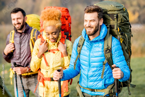 Multi ethnic friends in colorful jackets hiking with backpacks in the forest