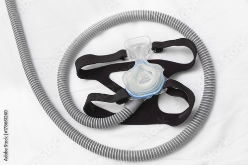 CPAP headgear mask, connecting with strap and hose laying on a bed, for helping people with respiratory problem