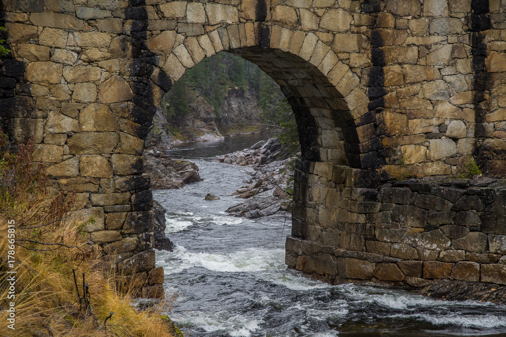 A beautiful historic stone bridge crossing the river in central Norway. Colorful autumn landscape. A beautiful historic stone bridge crossing the river in central Norway. Colorful autumn landscape.