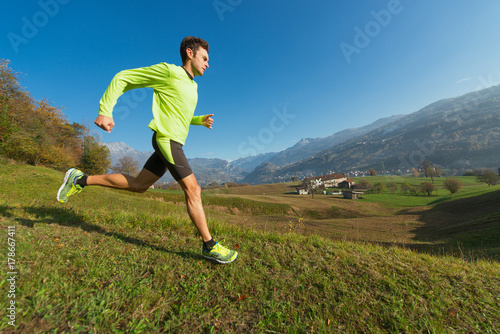 Athlete runs downhill in the meadow in a valley of the Italian Alps.