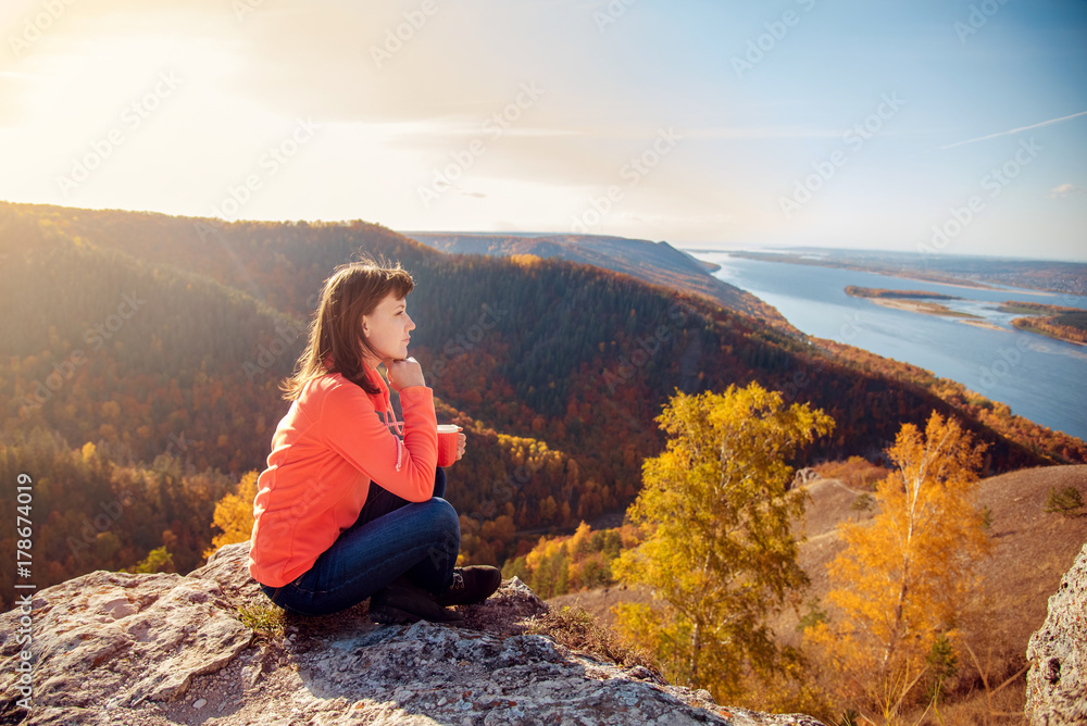 the girl is drinking tea on top of the mountain, holding a mug in her hands